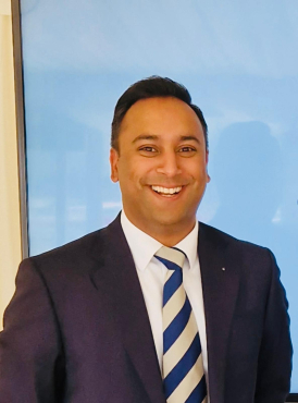 A headshot of Arun Photay in a navy suit and navy and silver tie.