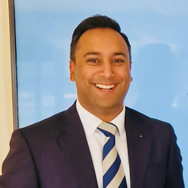 A headshot of Arun Photay in a navy suit and navy and silver tie.